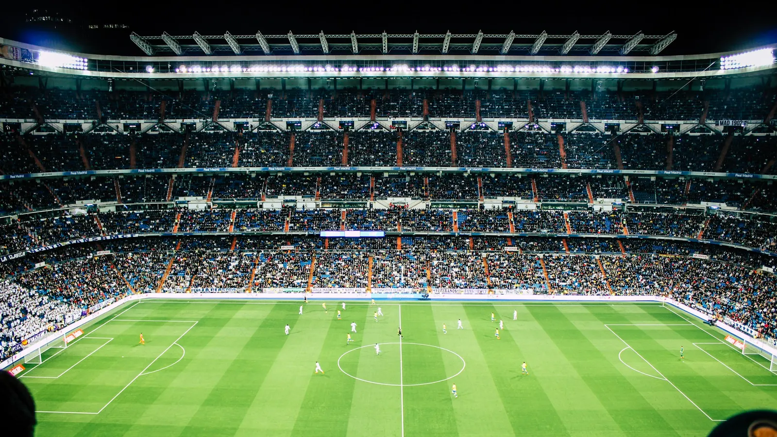 Tribunes d'un stade de football en pleine affluence, éclairées par les projecteurs lors d'un match en soirée.